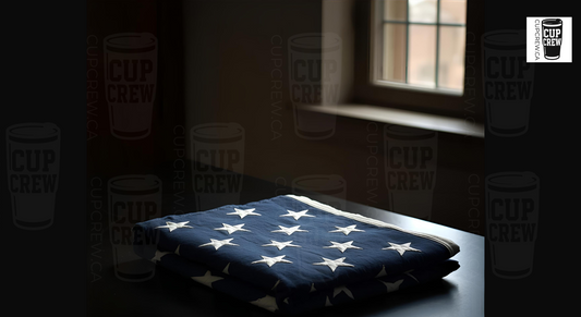 a folded American flag with white stars on a dark surface, with a window and cups with the word "CUP CREW" visible in the background.