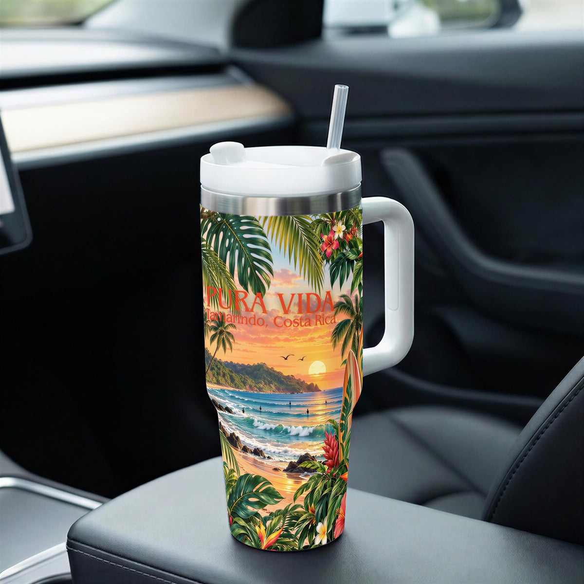 A colorful insulated tumbler with a tropical beach scene printed on it, sitting on the passenger seat of a car.