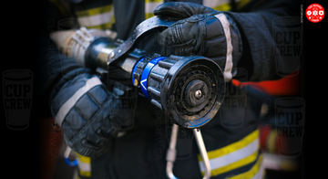 A close-up image of a firefighter's hand holding a fire hose, with the text "CUP CREW" visible on the gloves and the hose.