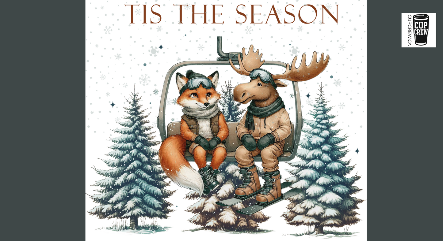 A fox and a moose are depicted on a ski lift, surrounded by snow-covered pine trees, with the text "TIS THE SEASON" above them.